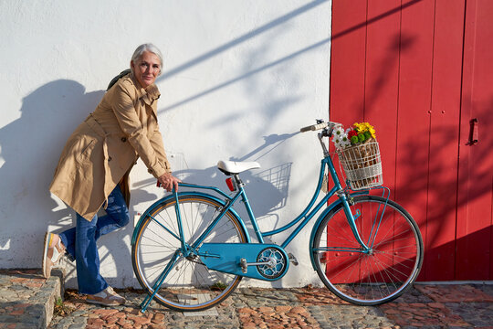 Woman leaning on bicycle standing in front of wall on sunny day