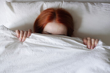 woman hiding face from sunlight under bed cover
