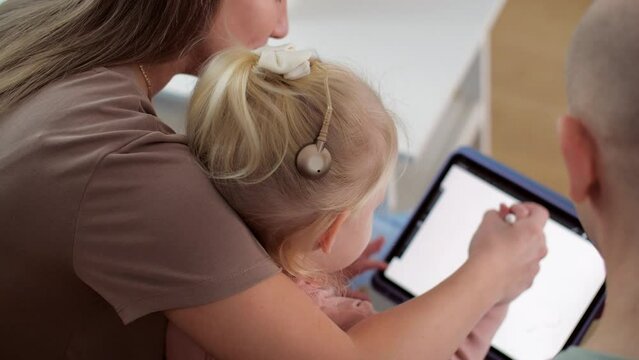 Kid with cochlear implants playing with tablet pc at home. Deafness and medical technology concept