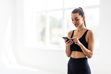 Fototapeta na wymiar Attractive healthy young woman with a fitness mat using mobile phone at the gym
