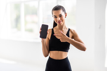 Sport, technology and active lifestyle concept. Satisfied attractive sportswoman pointing finger smartphone screen, recommend mobile workout tracker app