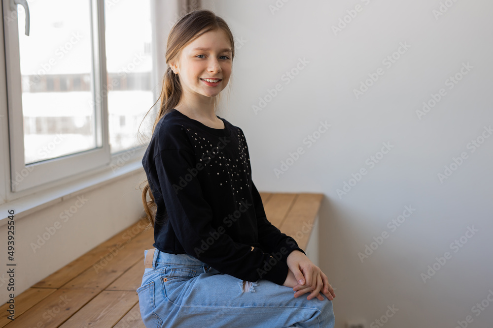 Wall mural caucasian teen girl sitting near a big window 