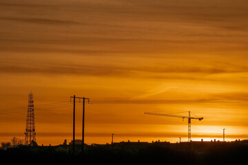 Fototapeta na wymiar Sunset of sunrise scene. Silhouette of a tall crane against warm orange color sky. Urban construction background. Calm mood.