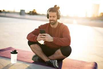 Young muscle man training outside. Fit handsome man listening the music while resting after training