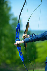 professional archer shooting with modern longbow in forest, close-up