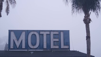 Retro neon sign of motel or hotel on road, foggy misty weather in California, USA. Palm trees in...