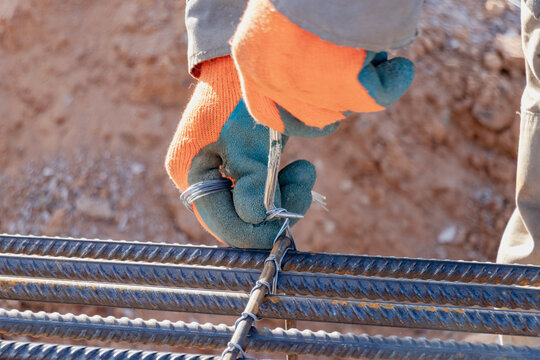 A worker uses steel tying wire to fasten steel rods to reinforcement bars. Close-up. Reinforced concrete structures - knitting of a metal reinforcing cage.