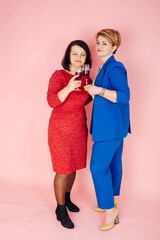 Studio shot Two middle-aged women drinking alcohol. Beautiful women with a glass of wine in their hands. Pink background