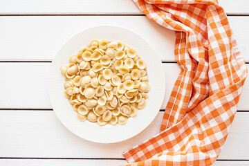 Dry uncooked orecchiette Italian pasta on white wooden background
