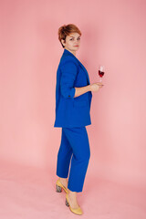 Elegant Ukrainian woman in a blue classic suit and yellow blouse on a pink background. Yellow and blue patriotic clothes. Woman with a glass of wine in her hands. Yellow shoes and blue trouser suit