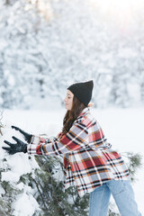 Young woman walks in forest, plays and takes snow from pine tree branch.