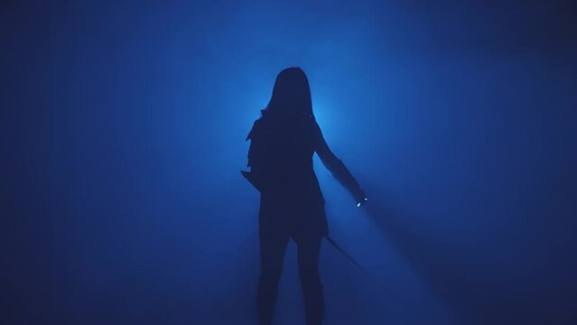 Dark silhouette fantasy woman warrior assassin holding two katana waving cuts air with weapon swords. Black background blue neon light full smoke. Fairy goddess warlife elf girl armed lady princess.