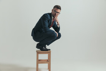 thoughtful businessman in suit holding elbows on knees and thinking