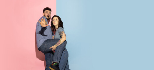 Portrait of young emotional man and girl isolated on blue and pink trendy color background. Human emotions concept