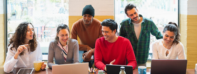 Horizontal banner or header multiracial group of young people working around computers with positive, smiling faces.