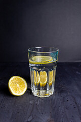 Glass of water with lemon cut on halfs on black table