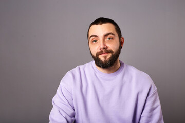 Happy bearded man wears violet sweater on grey background. friendly smile. Copy space