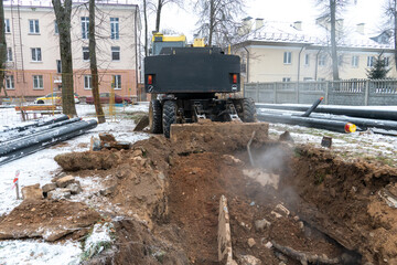 The excavator is working on the construction site to replace the pipeline in winter. Digging holes for laying new pipes for central heating in a residential area.