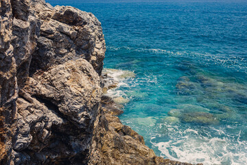 Wonderful views of the blue Mediterranean Sea. Sunny rocks, waves with foam and splashing water. The wave crashes into the rocks on the shore