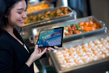 Portrait of a happy Asian woman holding a tablet with a smile on a blurred background of buffet food