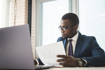 A black African American businessman in a business suit works at a laptop. Analytics and work online