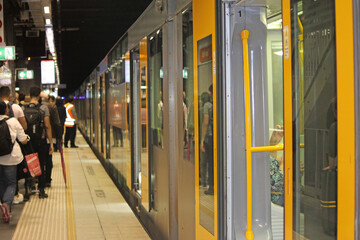 Yellow and grey train with its doors open on a crowded platform in an underground tunnel. Wynyard...