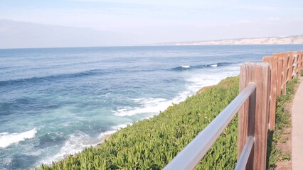 Ocean waves crashing on beach, sea water surface from above, cliff or bluff, La Jolla shore waterfront promenade, California USA. Succulent green ice plant, pacific coast. Seascape view and railings.