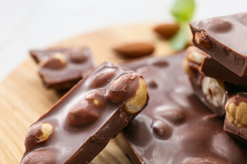 Pieces of tasty chocolate with hazelnuts on board, closeup