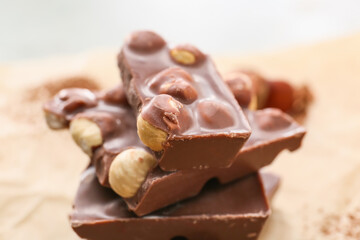 Pieces of tasty chocolate with hazelnuts on table, closeup