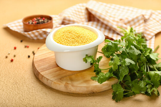 Bowl of raw couscous with parsley on color background