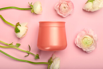 Jar of cosmetic product and beautiful ranunculus flowers on pink background