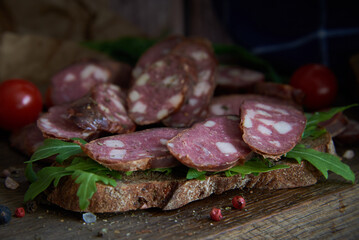 Sausage, cut into pieces, greens and tomatoes on a cutting wooden board.