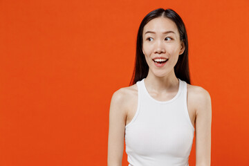 Excited vivid jubilant fascinating exultant fun young woman of Asian ethnicity 20s year old in white tank top looking aside keeping mouth wide open isolated on plain orange background studio portrait