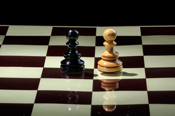 Black pawn chess piece standing face brown pawn chess piece