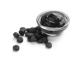 Bowl of activated carbon mask and pills on white background