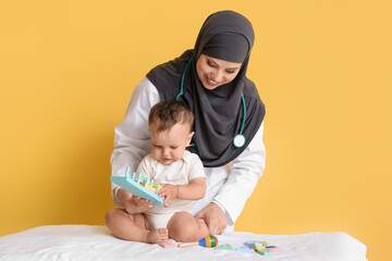 Muslim pediatrician examining baby boy on color background