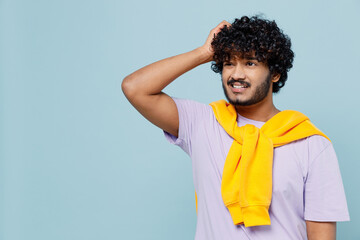 Puzzled confused perplexed young bearded Indian man 20s years old wears white t-shirt looking aside think put hand on head have no idea isolated on plain pastel light blue background studio portrait.