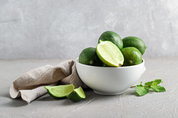 Bowl with fresh limes on grey background