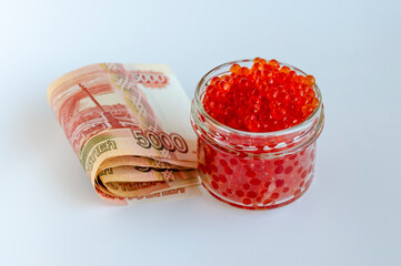 Red caviar in a glass jar and Russian money on a white background