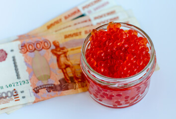 Red caviar in a glass jar and Russian money on a white background