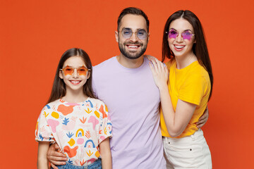 Young stylish smiling happy parents mom dad with child kid daughter teen girl in basic t-shirts colored glasses look camera isolated on yellow background studio portrait Family day parenthood concept