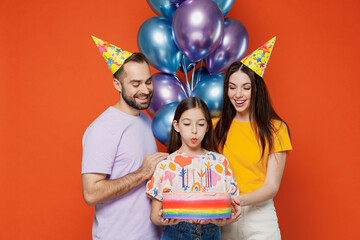 Young parents mom dad with child kid daughter teen girl wear basic t-shirts birthday hat hold cake with candles blow candles making wish isolated on yellow background. Family day childhood concept
