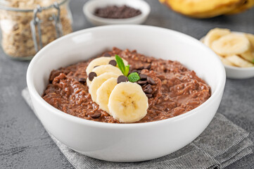 Chocolate oatmeal porridge with banana and chocolate chips on top in a white bowl. Healthy...