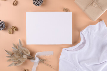 Baby shower invitation 7x5 boho card mockup with baby bodysuit and boho decotation on neutral beige background, minimal bohemian baby shower blanck mockup, greeting card mockup, modern newborn card