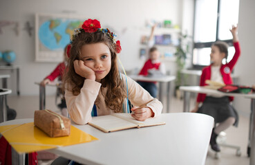 Little sad Ukrainian girl sitting in classroom during class, concept of enrolling Ukrainian kids to...