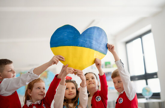 Little schoolchildren holidng heart in Ukrainian colors in classroom, no war concept.