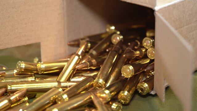223 caliber bullets - Poured out from cardboard box and laying on camouflage military jacket - Slider right to left