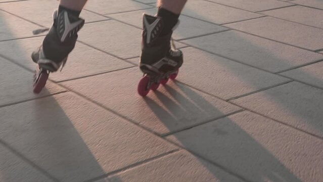 Slow motion, close up on person's feet roller blading on pavement during golden hour. No face