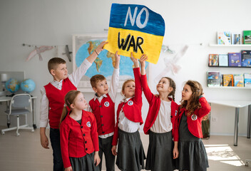 Little schoolchildren holidng and showing ukrainian flag in classroom, no war concept.