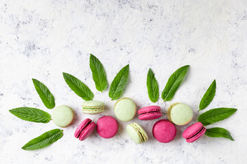 Design of green and pink macarons with mint leaves on white background. Traditional French sweet dessert.